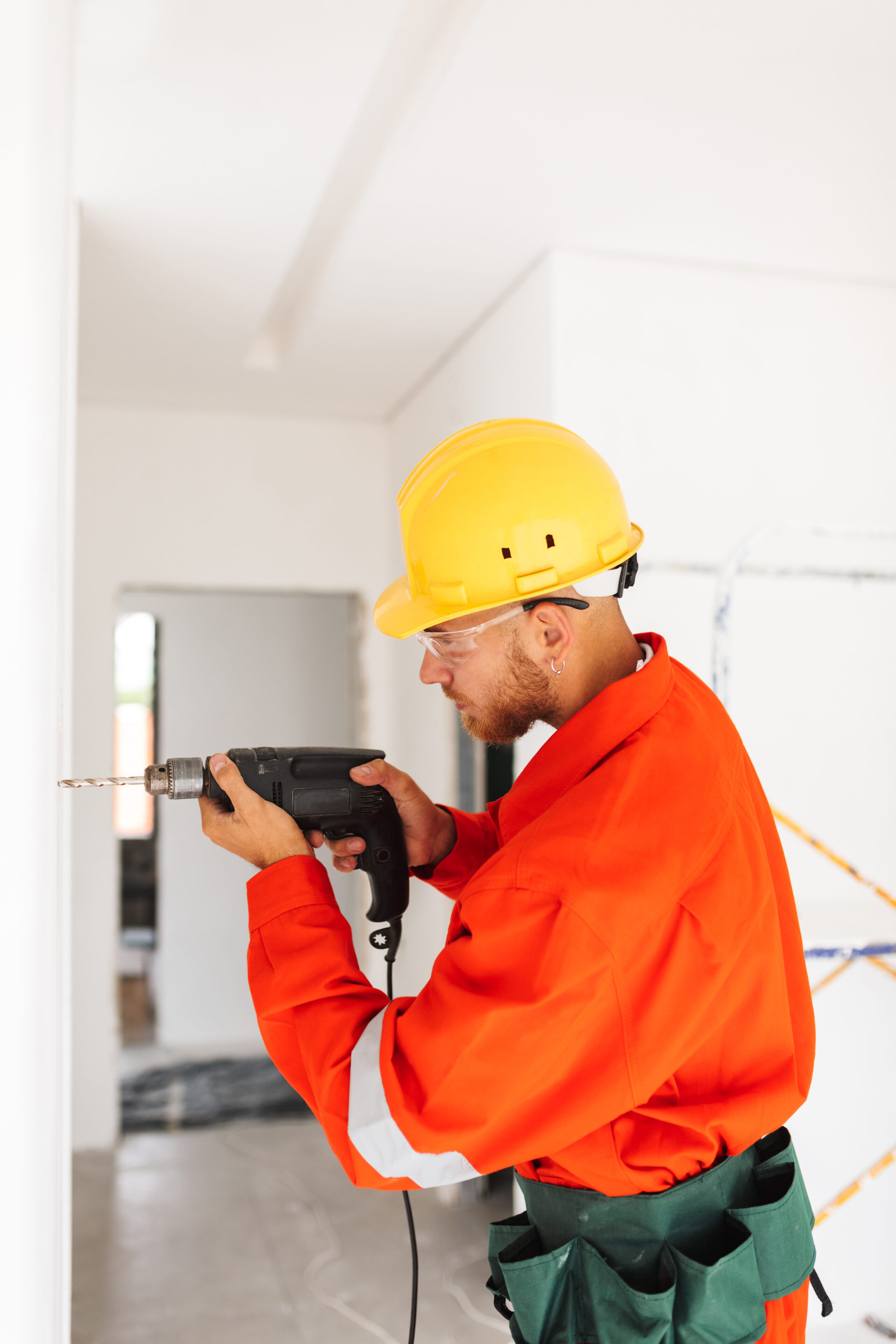 young builder in orange work clothes and yellow hardhat using el